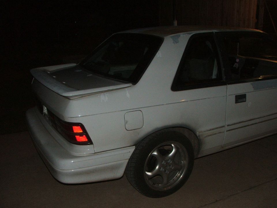 White Dodge Shadow coupe, rear passenger side view, parked at night.