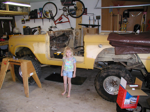 1971 Ford Bronco - A young girl stands next to a yellow 1971 Ford Bronco that is undergoing repairs in a garage.