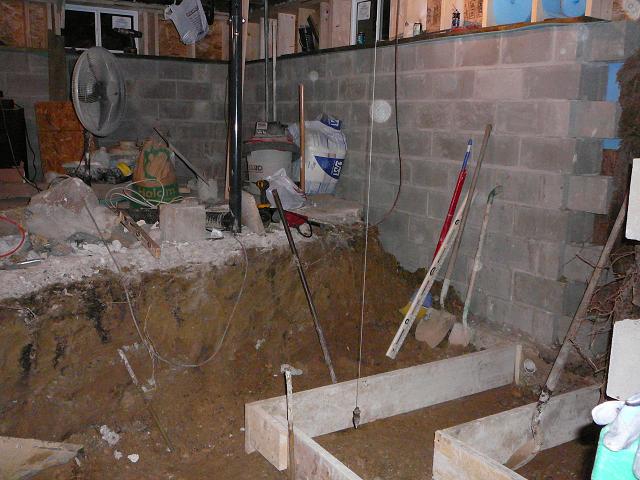 Construction scene in a basement with concrete block wall and dug-out area.