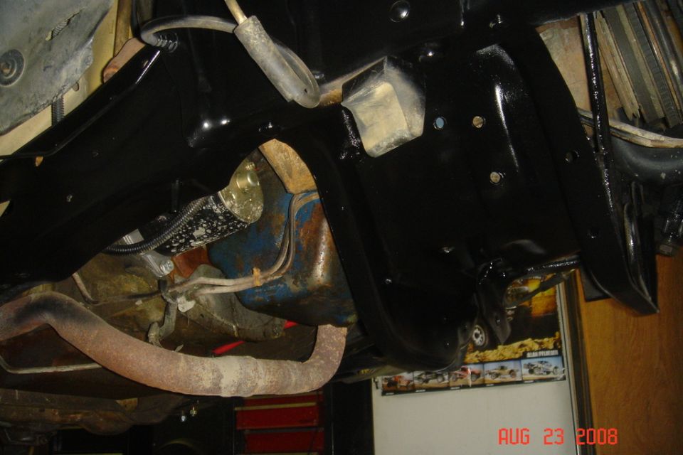 Underside of a vehicle showing black frame, rusty exhaust, and blue oil pan.