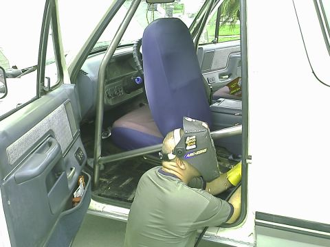 1990 Ford Bronco - A person wearing a welding mask works on the interior of a vehicle, likely a Ford Bronco, with a roll cage installed. The driver's side doo…