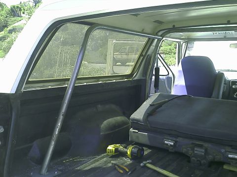 1990 Ford Bronco - Interior view of a 1990 Ford Bronco showing a custom roll cage installed in the rear cargo area. Tools and a large black case are also visi…