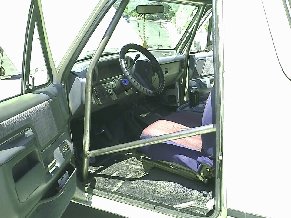 Interior of a 1990 Ford Bronco with roll cage, blue and pink seat, and dashboard.