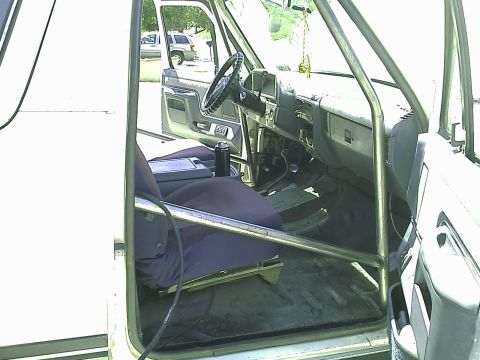 1990 Ford Bronco - Interior view of a white 1990 Ford Bronco showing the driver's side seat, dashboard, steering wheel, and a roll cage. The vehicle appears t…