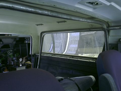 1990 Ford Bronco - Interior view of a vehicle's roll cage and seats, with a glimpse of a garage scene and the outdoors through the rear window.