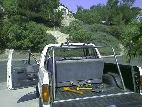 1990 Ford Bronco - The open driver's side door of a white Ford pickup truck reveals a blue interior. A roll bar is installed behind the cab, and the truck bed…