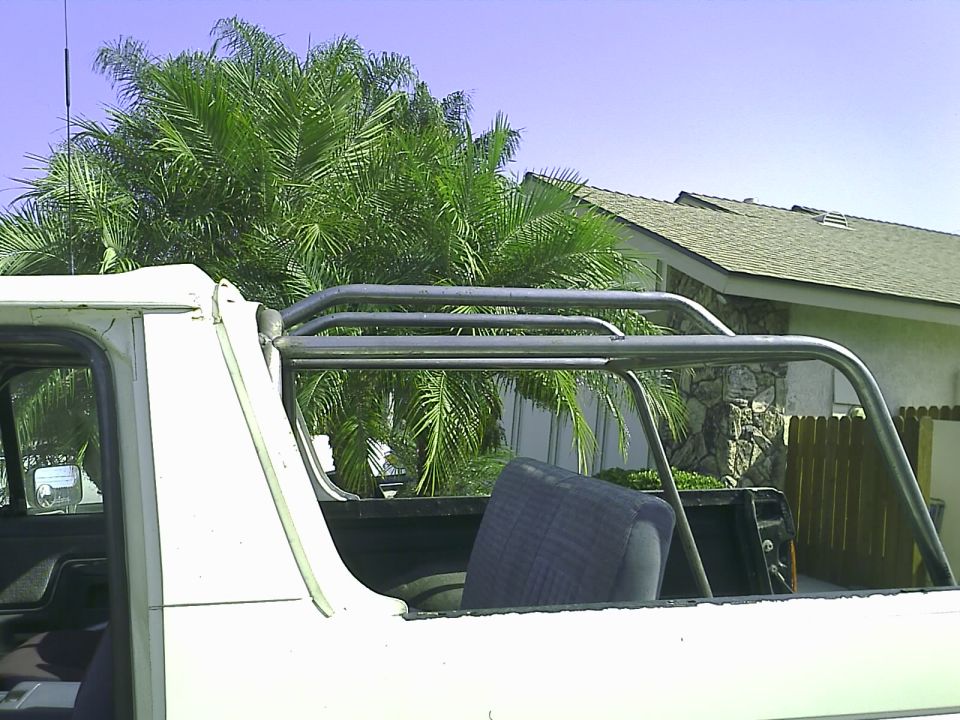 White 1990 Ford Bronco with roll cage, rear passenger side view.