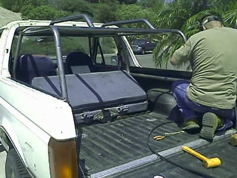 1990 Ford Bronco - A man in a green shirt and blue jeans works on the roll cage of a white 1990 Ford Bronco. The Bronco is a convertible with the top removed,…