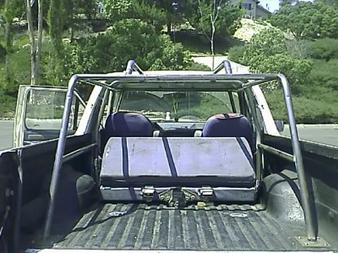 1990 Ford Bronco - Rear view of a 1990 Ford Bronco with the doors open and a large gray case in the bed. The vehicle has a silver roll cage installed over the…