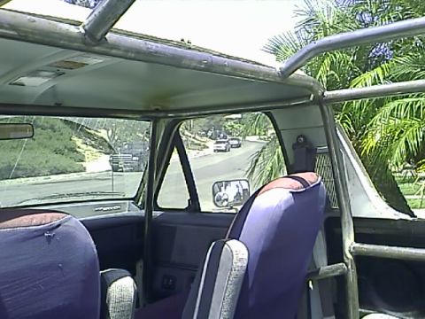 1990 Ford Bronco - Interior view of a modified 1990 Ford Bronco showing custom roll cage, purple seat covers, and a view of the road and palm trees through th…