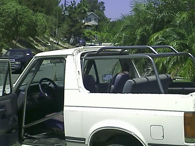 White Ford Bronco with top removed and roll cage exposed parked outdoors
