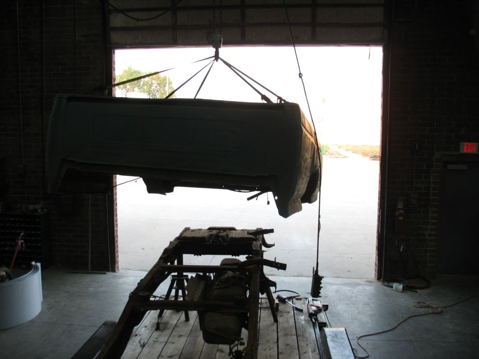 Pickup truck bed suspended by hoist above its disassembled frame in a garage.
