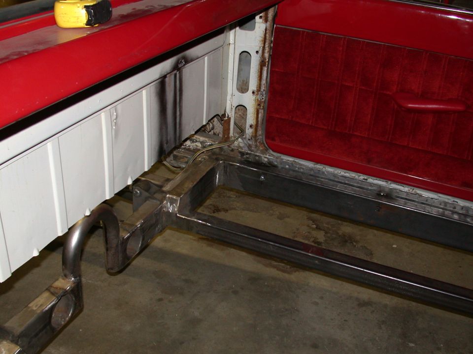 Restoration of red vehicle showing bare metal frame rails, exhaust pipe, and red velour interior panel