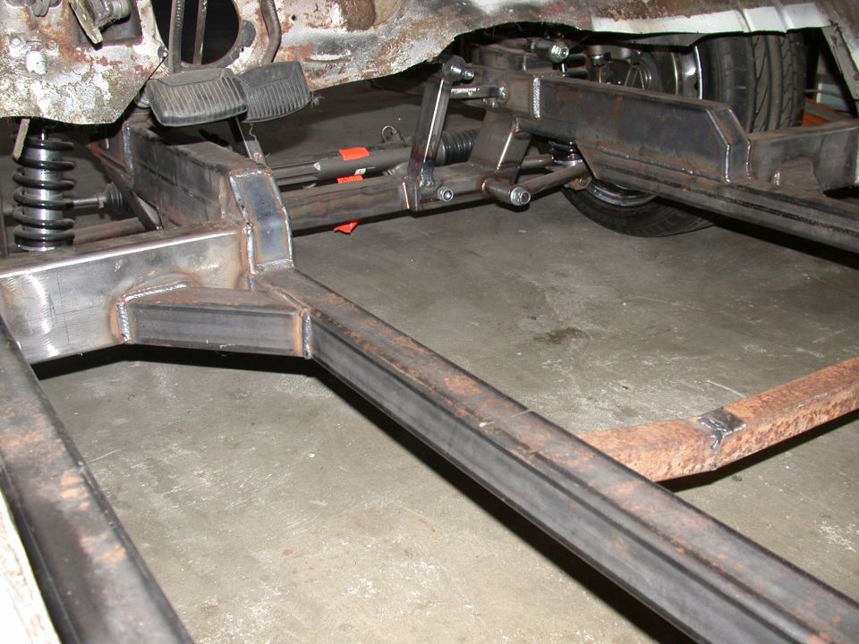 Underside of vehicle frame showing welded steel crossmember, suspension and steering components