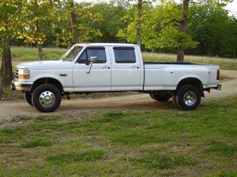 1972 Ford Bronco - This white dually pickup truck is seen from the side, parked outdoors on a dirt path.