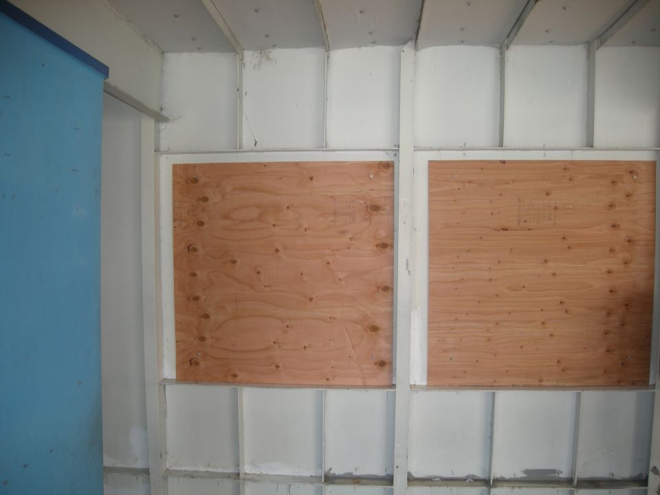 Interior of a building with two large plywood sheets covering window openings. A blue panel is on the left