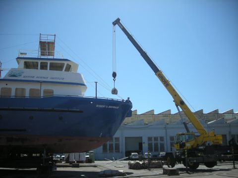 1991 Ford Bronco - A large boat is being lifted by a crane at what appears to be a shipyard or dry dock.