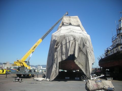 1991 Ford Bronco - A large object, possibly a boat, is covered by a tarp and being worked on by a crane.