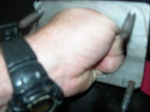 1984 Ford Bronco - A hand wearing a black watch is shown holding a tool near a metal plate.