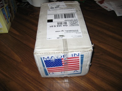 1995 Ford Bronco - A cardboard box sits on a wooden floor, covered in shipping labels and an American flag sticker indicating it was made in the U.S.A.