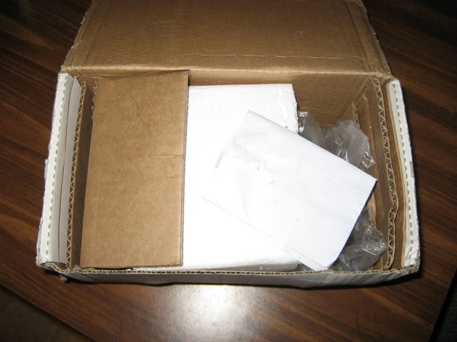 Open cardboard box containing brown cardboard inserts and white paper. Some plastic wrap is also visible