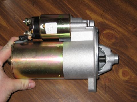 1995 Ford Bronco - A starter motor part is displayed against a wooden background, with a hand holding it.
