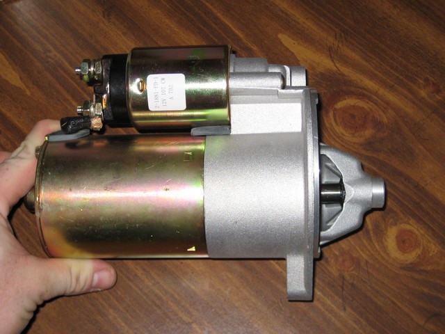 Starter motor held in hand, showing gold and silver metal components and electrical terminals