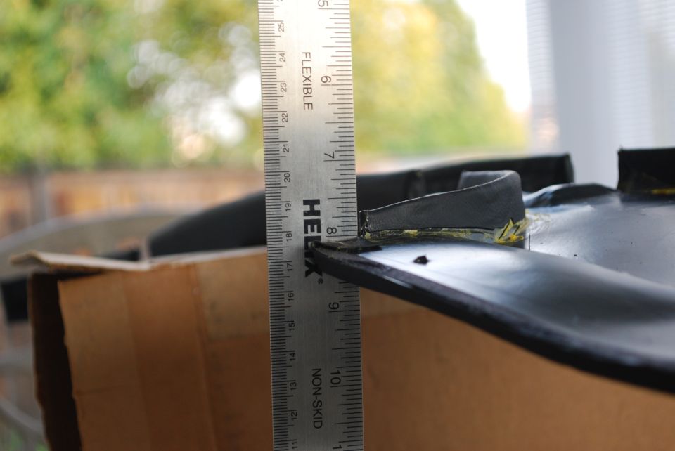Black car part with a ruler measuring its height against a cardboard box