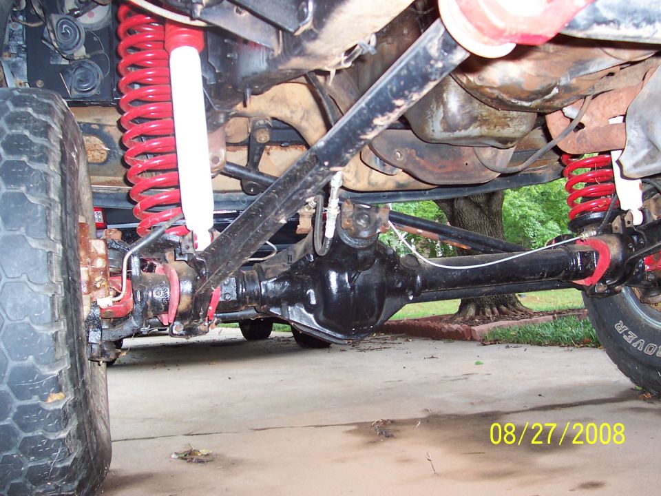 Undercarriage of a vehicle with red coil springs and white shocks, showing the rear axle and suspension components