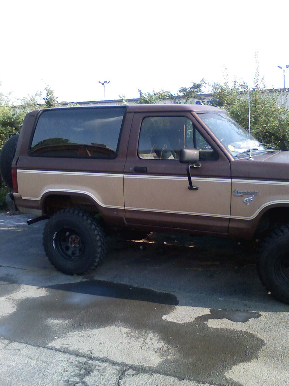 Brown and tan Ford Bronco II, lifted with off-road tires. Spare tire mounted on rear
