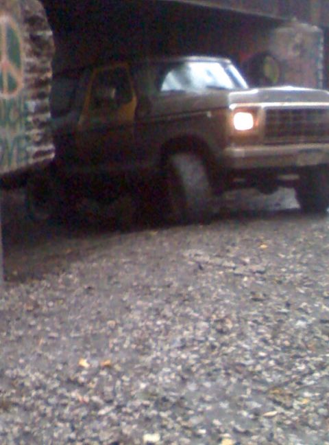 1979 Ford Bronco - A dark brown 1978 Ford Bronco is parked on a gravel surface, with its front passenger side illuminated by its headlight.