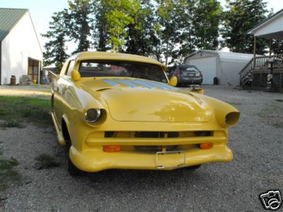1953 Ford Mainline - A heavily modified yellow coupe sits in a gravel driveway with a house and garage in the background.