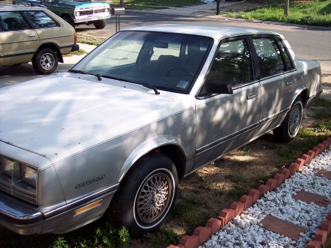 1972 Ford Ranchero - A silver sedan with a two-tone paint scheme is parked on a street, with other vehicles visible in the background.