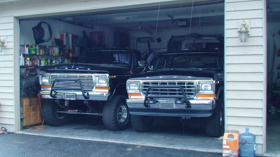 Two black 1979 Ford F-250 pickup trucks parked side-by-side in a garage