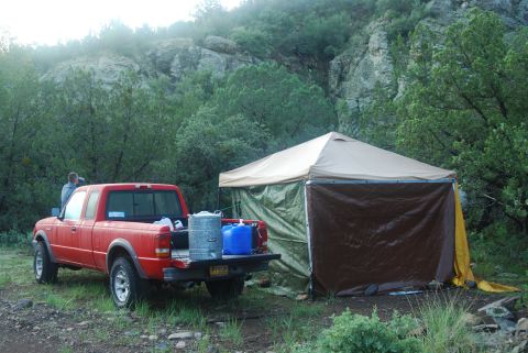 1997 Ford F-250 - A red pickup truck is parked beside a camping tent in a wooded area.