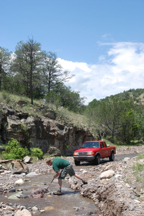 1997 Ford F-250 - A red pickup truck is parked on a dirt road next to a stream where a person is wading.