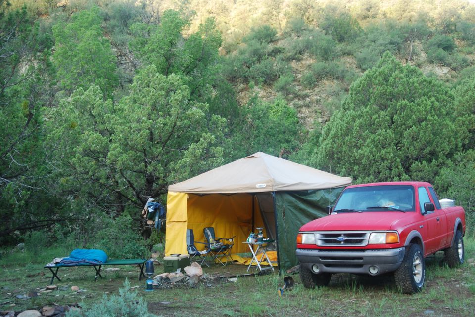 Red pickup truck parked next to a camping tent in a wooded area