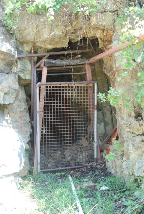 1997 Ford F-250 - A mine entrance is secured by a metal grate and wooden beams, set into a rocky hillside.