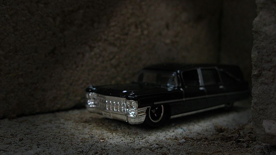 Black die-cast Cadillac hearse model with chrome grille in dim light