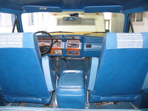 1984 Ford Bronco - The interior of this vehicle features blue upholstery, a wood-grain dashboard, and a center console cooler.