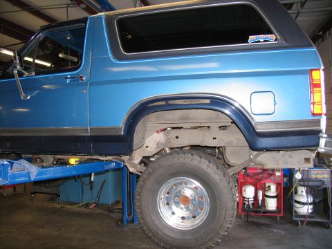 1984 Ford Bronco - Blue SUV on a lift, revealing its undercarriage and rear wheel assembly.