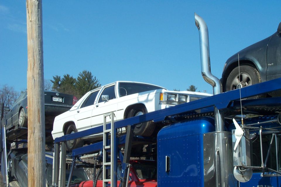 White Ford Crown Victoria loaded on the upper deck of a blue car-hauler trailer