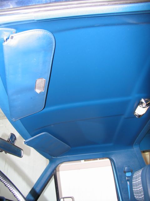 1984 Ford Bronco - The interior of a vehicle shows a blue headliner with two sun visors and a dome light fixture.