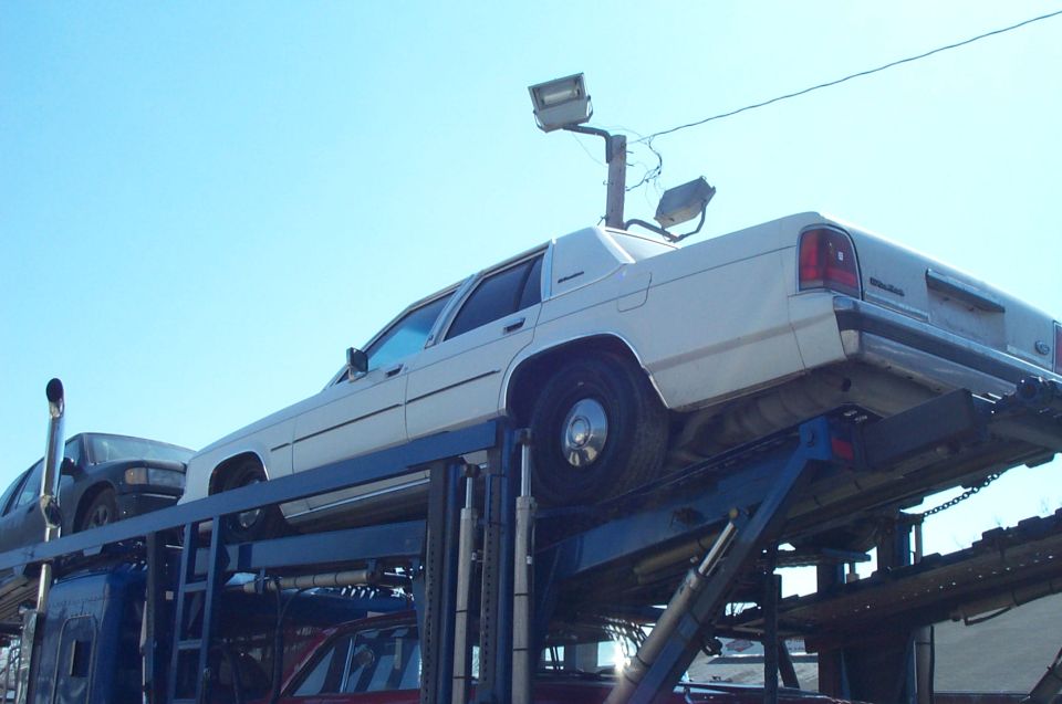 White Ford Crown Victoria strapped to raised upper deck of a car-hauler, low rear angle