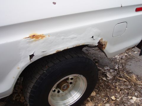 1979 Ford Bronco - The rear quarter panel of a white vehicle displays extensive rust damage around the wheel well.