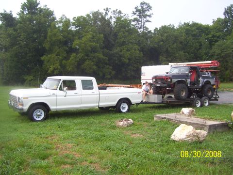1978 Ford Bronco - A white 1978 Ford F-Series crew cab pickup truck tows a trailer carrying a modified black Bronco on a grassy lot.