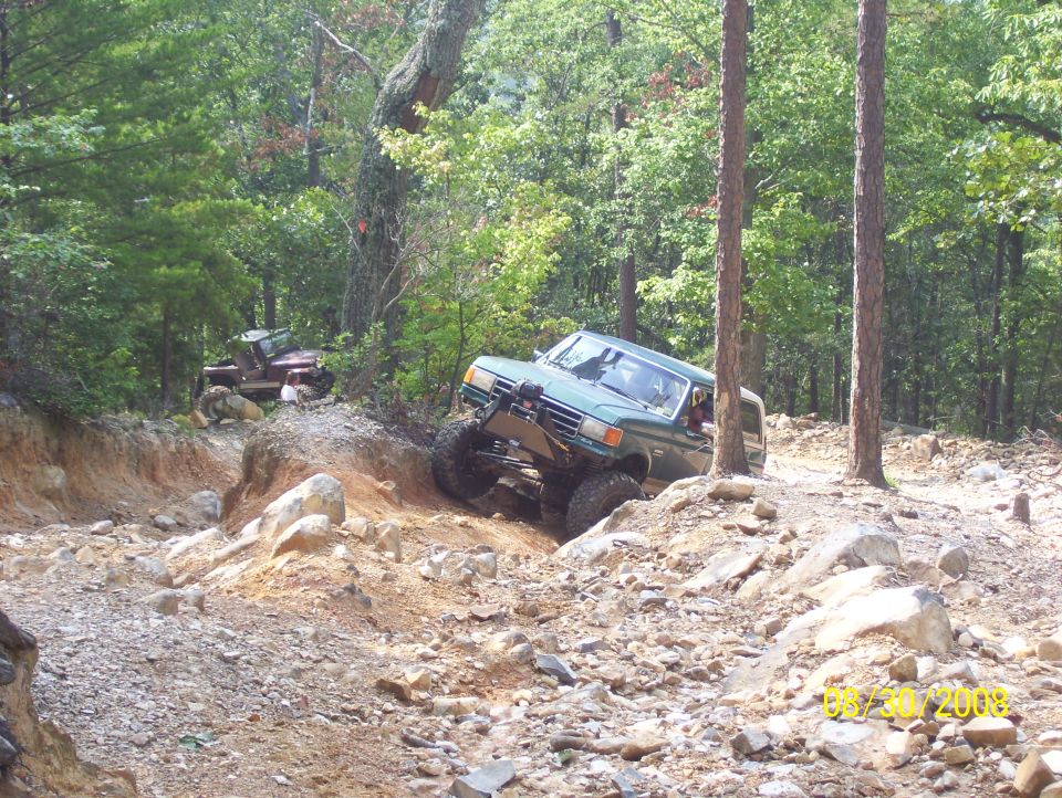 Green off-road vehicle climbing a rocky hill with another vehicle behind it