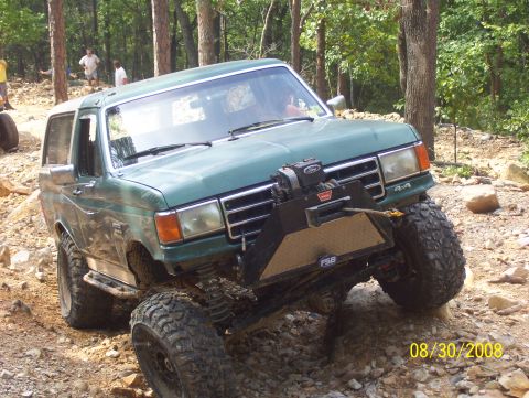 1978 Ford Bronco - This green SUV, likely a 1987 Ford Bronco, navigates a challenging off-road course with its winch and large tires.