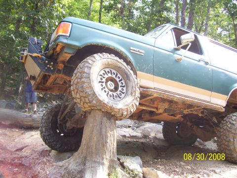 1978 Ford Bronco - Green Ford Bronco navigates a difficult off-road obstacle on a wooded trail.
