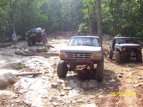 1978 Ford Bronco - Off-road vehicles navigate a challenging rocky path in a wooded area.